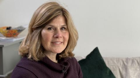 Cristiana in a purple jumper sitting on her sofa.