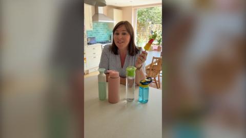 Catherine Burne holds an ice lolly in a kitchen with water bottles