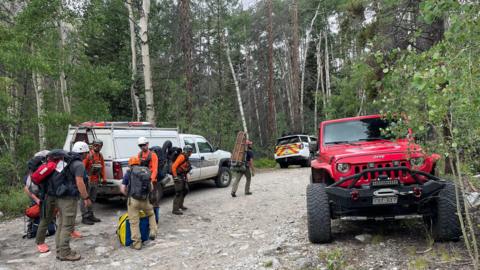 A group of rescuers stand next to vehicles in a mountainous area