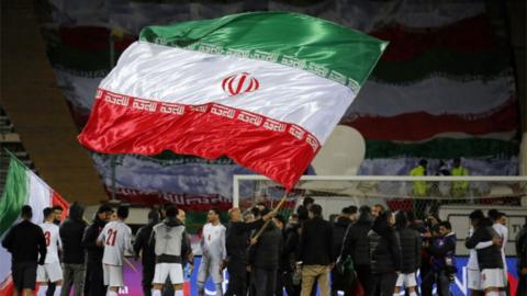A giant flag of Iran, waved on a football pitch.