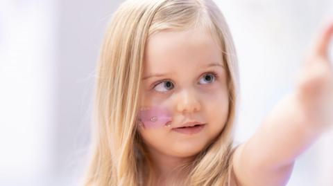 A close up of Seren who has blue eyes and long, blonde hair. She is pointing at something.