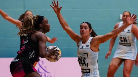 A London Pulse netball player holds a ball and is blocked by an opponent