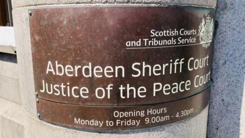 A bronze sign outside Aberdeen Sheriff Court which says Aberdeen Sheriff Court Justice of the Peace Court.