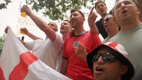 Group of England fans singing while holding England's flag