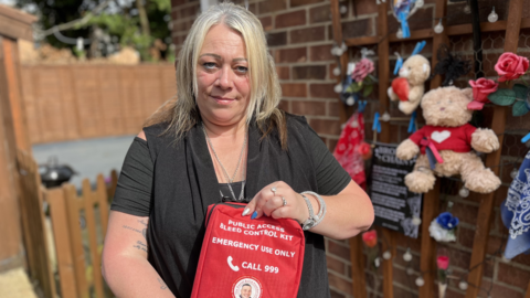 Margaret Oakes in a black top holding a bleed control kit which has a label that reads "Public access bleed control kit"