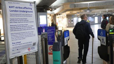 A man walks through a wide barrier next to a sign about Tube strikes