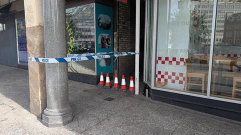 Police tape sealing a narrow alleyway between two shop frontages