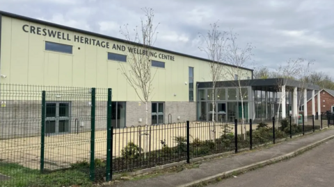 A green-grey building behind fencing on the side of the road