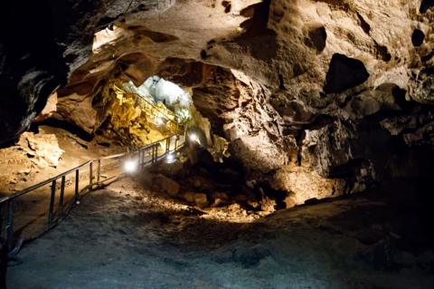 The image is of a large cavernous space. There is a walkway constructed on the left hand side with handrails and lighting. 