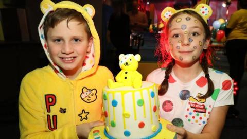 Two children hold a Childern in Need themed cake
