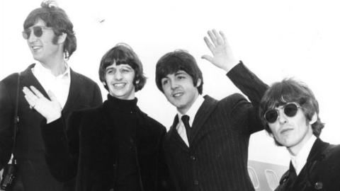 The Beatles wave goodbye from the steps of an aeroplane as they leave for a tour of America in 1966