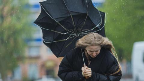 Stock photo of a blonde woman under umbrella during storm weather. Her black umbrella has blow inside out and she has her head down. 