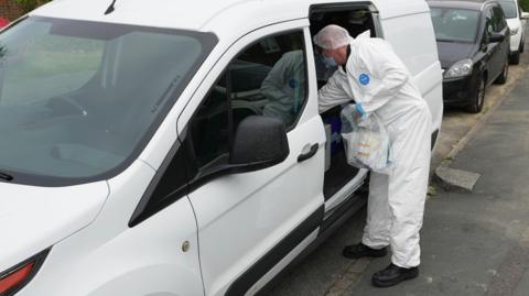 A person in a hazmat suit looking in a car