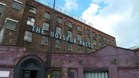 An old rebrick building with 'The Hotspur Press' attached to the front in large white letters