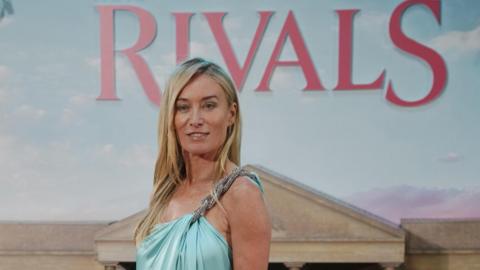  Victoria Smurfit arriving for the world premiere of season two of Rivals, at BFI IMAX in Waterloo, central London. She has long blonde hair, wearing a light blue gown. A sign for Rivals is behind her.
