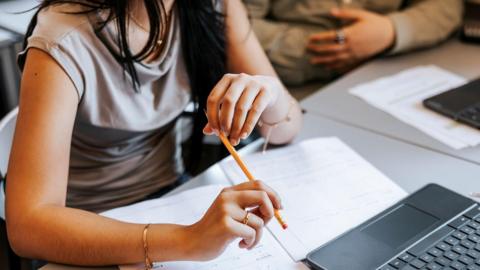 High school pupils sitting at desks. There are work books and laptops on the desks.