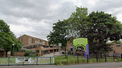 A red brick shopping centre with a green and purple sign in front