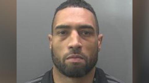 Daniel Findlay's custody image. He is wearing a black and grey striped fleece.