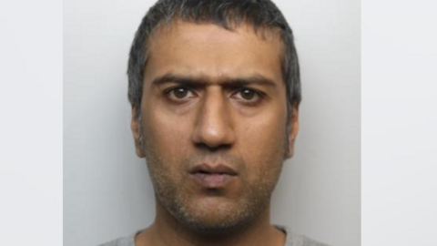 Janaed Akhtar frowns at the camera in a police custody photo. He has short, grey hair and stubble.