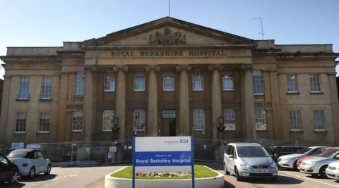 The front facade of Royal Berks hospital. It looks greek-esque with classical pillars at the front. There is a full carpark in front