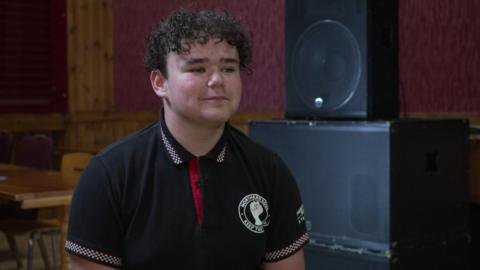 Keiven pictured being interviewed. He is wearing a black polo shirt with two-tone detail on the sleeves and collar.