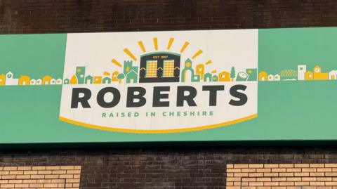 Picture of the Roberts signage outside their Northwich factory. The logo which is green and yellow reads 'Roberts - Raised in Cheshire'.