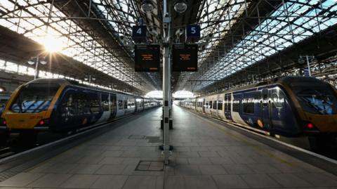 Two Northern trains sit parked at the platforms of Manchester Piccadilly station.