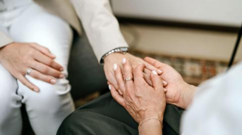 A woman opposite another holding her hand. Only the hands and forearms are visible.