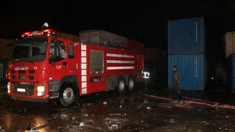 Fire engine and fire fighter beside shipping containers set on fire by suspected Israeli strike on Lataka port, Syria (7 December 2021)