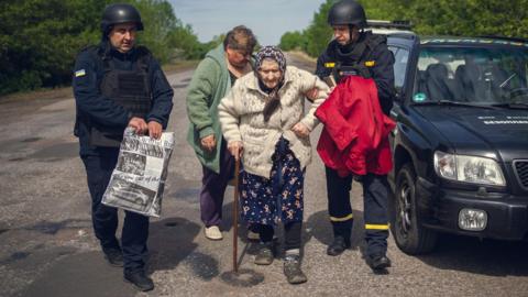 An elderly Sumy region resident is evacuated from her village with the help of two men