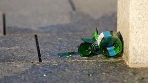 Stock image of a broken green beer bottle lying on a pavement.