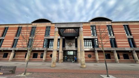 Exterior of Teesside Crown Court. It is a large imposing three-storey building made from red brick with long dark windows and four giant columns supporting a glass roof above the porch.