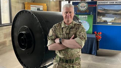 Flt Lt Ady from 617 Squadron, in uniform, standing in front of the replica bouncing bomb