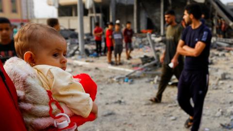 A person holds a baby as Palestinians gather at the scene of a reported Israeli air strike in Khan Younis, in the southern Gaza Strip (23 October 2023)