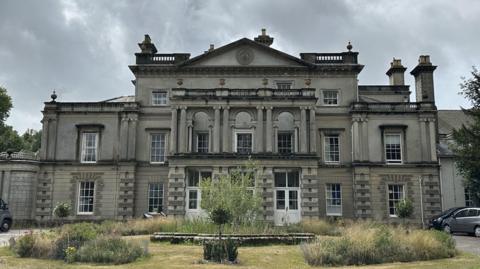 A large mansion-style home is pictured which is the home of Brainkind. A grassed area sits in front of the house. 