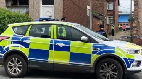 A police car in front of cordoned off alleyway with police officers visible behind it