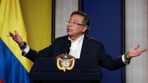 Colombian President Gustavo Petro gesticulates as he  speaks during a press conference. He wears a white shirt and dark jacket.