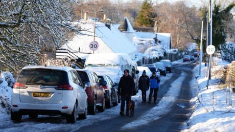 A rural street covered in snow and cars parked 