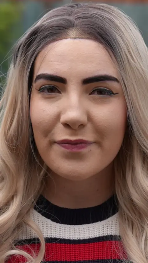 A woman with blonde hair wearing a white and blue top
