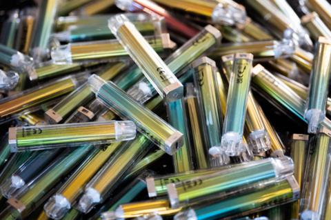 A pile of disposable vapes. They are blue, green and gold.