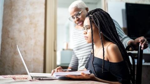 A teenage women uses her laptop to revise with a parent alongside her