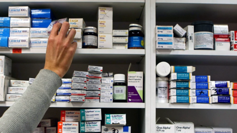 Pharmacy shelf with a hand reaching up for some medicine