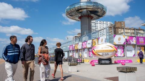 Four people walk past the i360 on Brighton sea front 