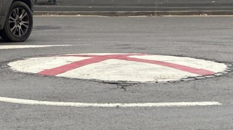 A mini roundabout covered with paint in the style of the Cross of St George flag
