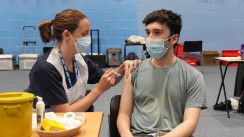 Man wearing face mask receives vaccine from nurse, who is also wearing a face mask