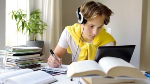 GCSE chemistry image: a student with textbooks, a laptop and headphones revises for chemistry.