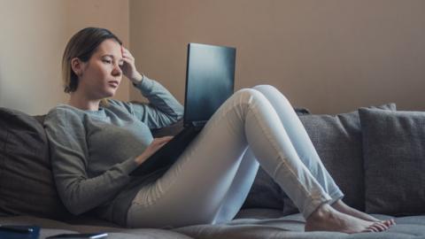 Woman sitting on sofa and looking for a job on her laptop
