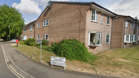 A Google Street View image of the entrance to the Eagle House Gardens, a residential street. There are a number of terraced houses and a sign which reads "Eagle House Gardens".