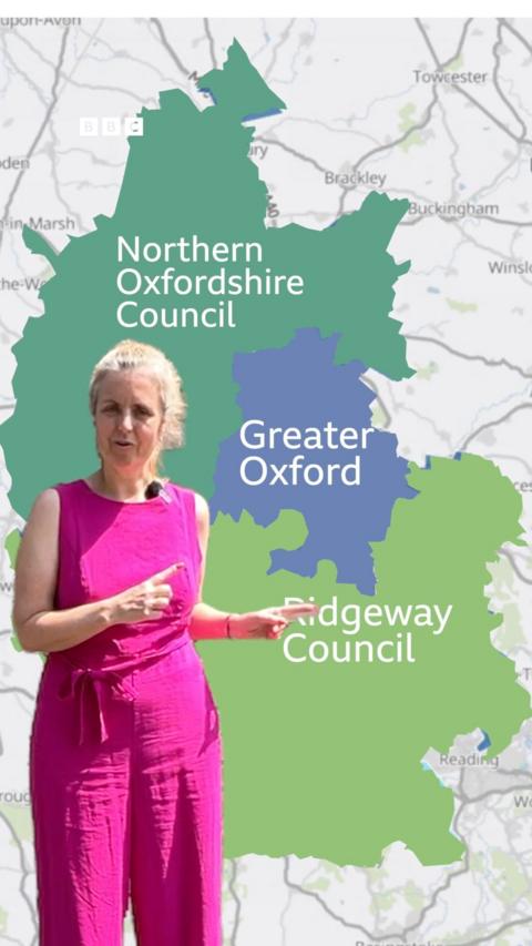 A woman in a pink outfit stands in front of a map of Oxfordshire.