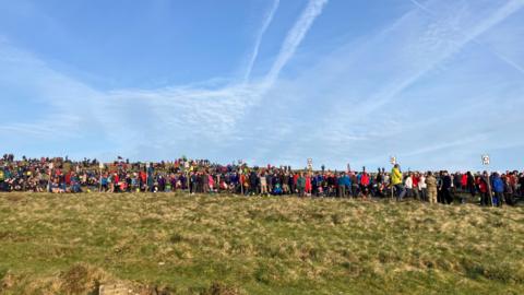General view of participants setting off at Ten Tors in 2025. Hundreds of participants are stood in a long line on a grass field.